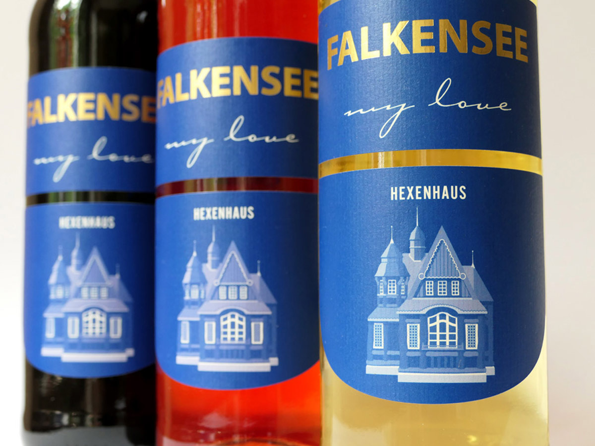Nahaufnahme der Weinetiketten „FALKENSEE my love“ mit goldener Schrift und Hexenhaus-Grafik – Design: Isabel Gewecke.