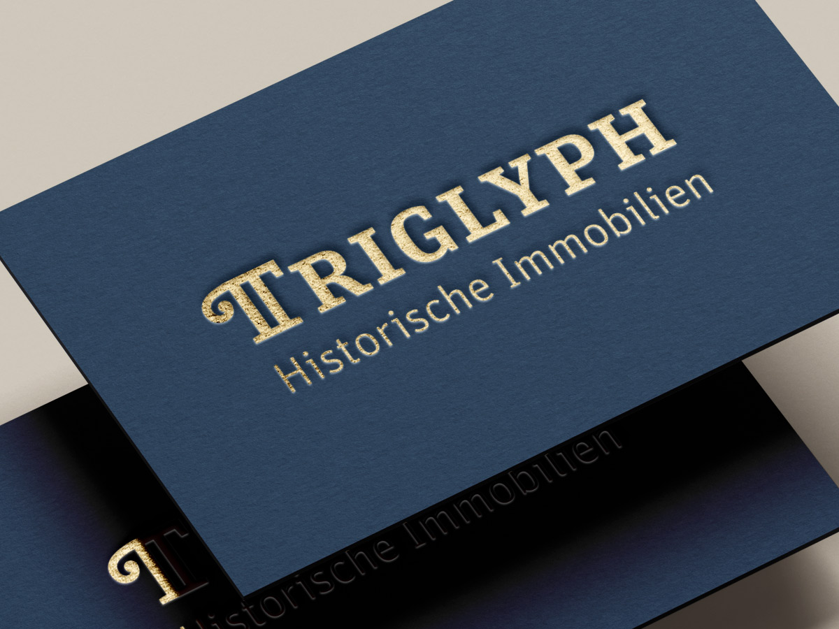 Dunkelblaue Visitenkarte „TRIGLYPH Historische Immobilien“ mit goldener Prägung im Close-up. Design: Isabel Gewecke